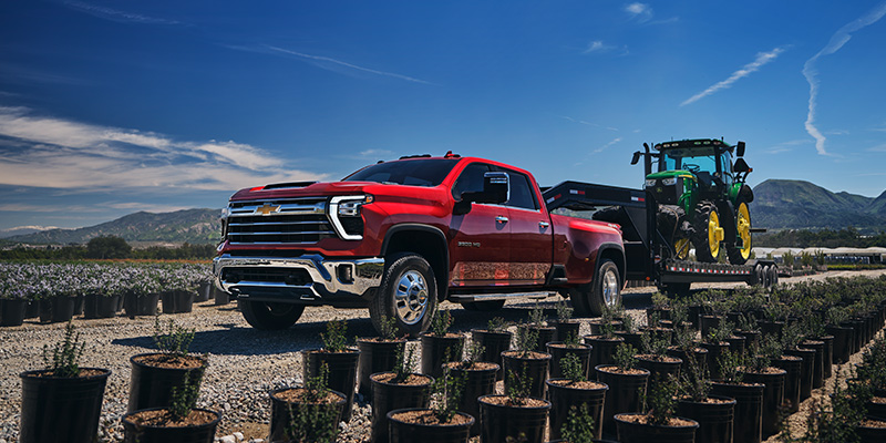 A 2025 Chevrolet Silverado 2500 HD hauling a tractor through a tree farm in Carthage, MS